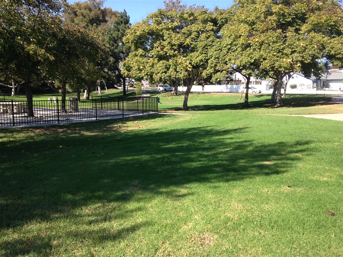 Sea Canyon Park with a grassy area, trees providing shade, and a fenced-off section on the left side. 