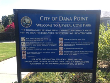 Blue sign reading ‘City of Dana Point – Welcome to Crystal Cove Park’ with park rules and regulations listed below.