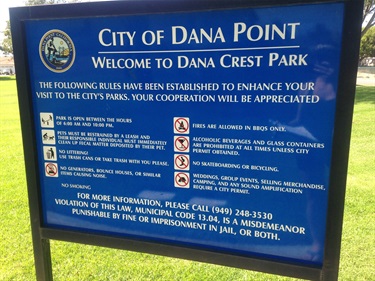 Blue park sign in Dana Point with city seal, welcoming visitors to Dana Crest Park and listing park rules.