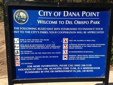 Blue sign at Del Obispo Park in Dana Point listing park rules and regulations.
