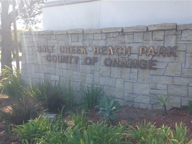 Stone wall sign with raised letters reading “Salt Creek Beach Park, County of Orange,” surrounded by green plants and landscaping.