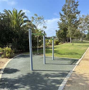 Outdoor fitness equipment along Sycamore Creek Trail, adjacent to a paved path, grassy lawn, and mature trees.