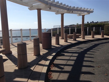 Bluff top trail curved walkway with columns and pergola overlooking water on a sunny day